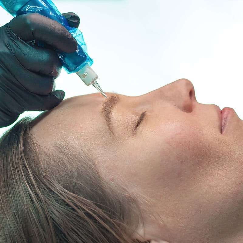 Eyebrow tattoo procedure with a machine on a client