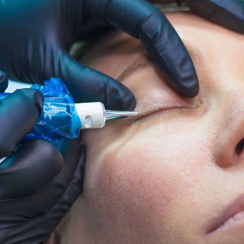 Permanent eyeliner procedure with a machine on a client's eye