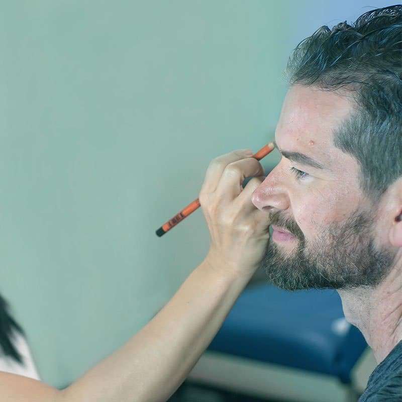 Permanent makeup artist mapping a male client's eyebrows with a pencil