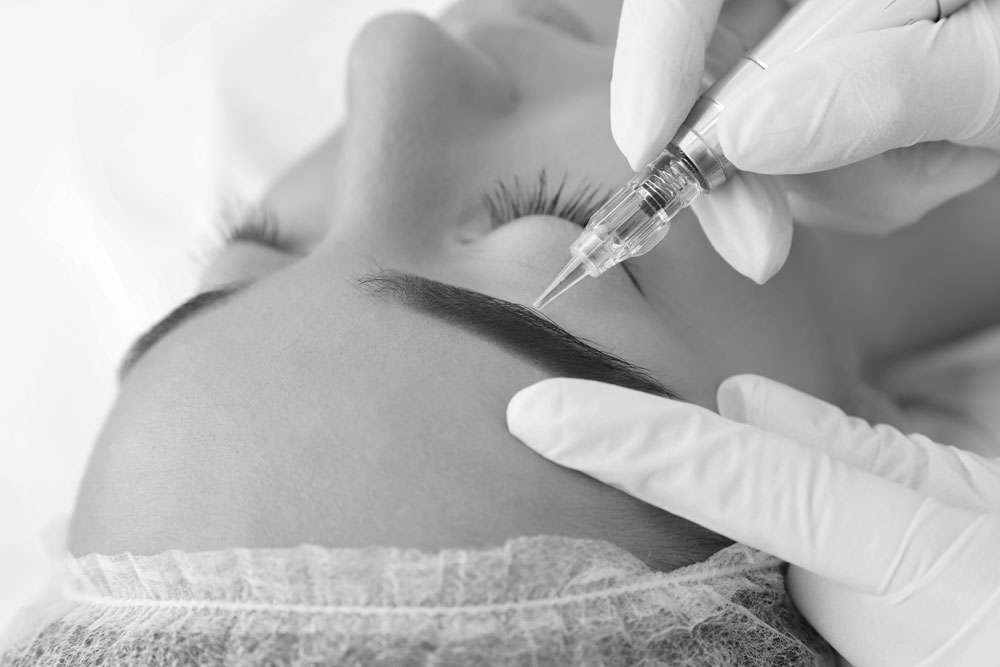 Black and white close-up of an eyebrow tattoo procedure with a machine on a client